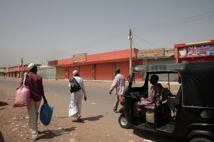 People carrying plastic bags of goods walk past shuttered shops in Khartoum.