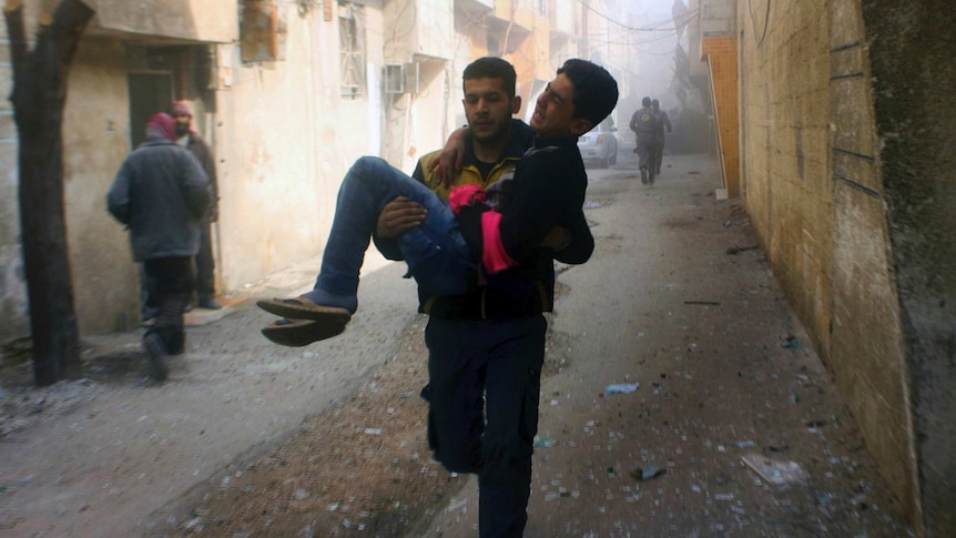 A man carries another man who was wounded during airstrikes through an alleyway.