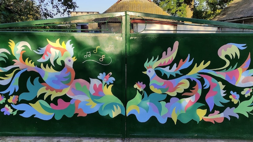 Two gates in green with colourful birds painted on them. Birds are singing and facing each other