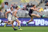 An AFL player is mid-air after kicking the ball clear, as defenders chase him.