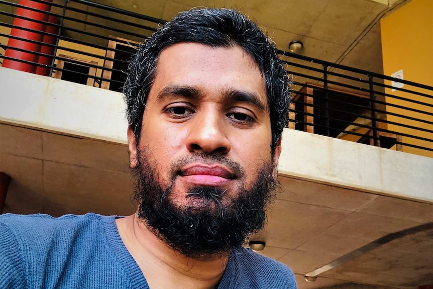 Selfie of man with beard looking at camera. Balcony or building behind.