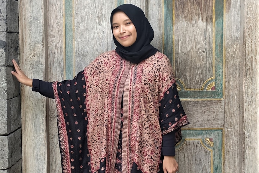 A woman in headscarf posing outside a door