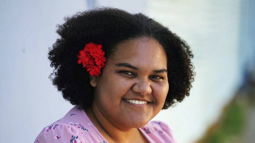 A young woman with a flower in her hair smiles and poses for a photo outside, finding balance after burn out.