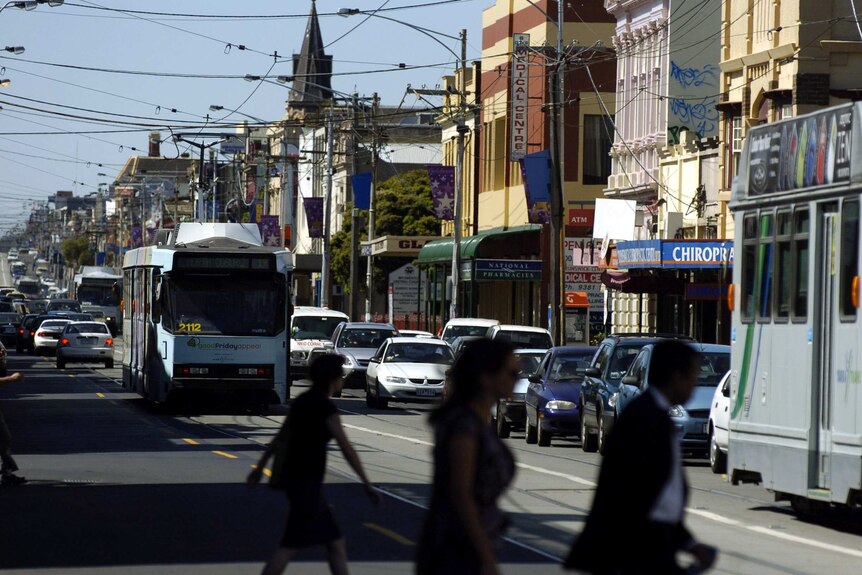 Three people crossing the road as a tram makes its way down Sydney Road, Brunswick