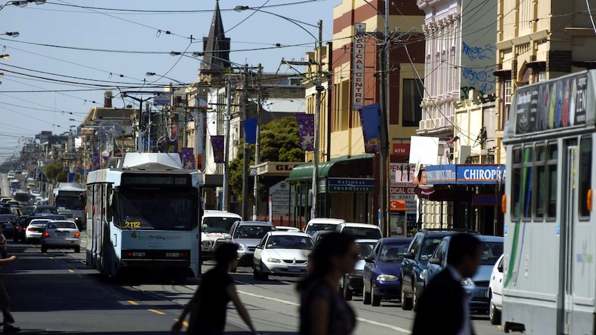 Three people crossing the road as a tram makes its way down Sydney Road, Brunswick.