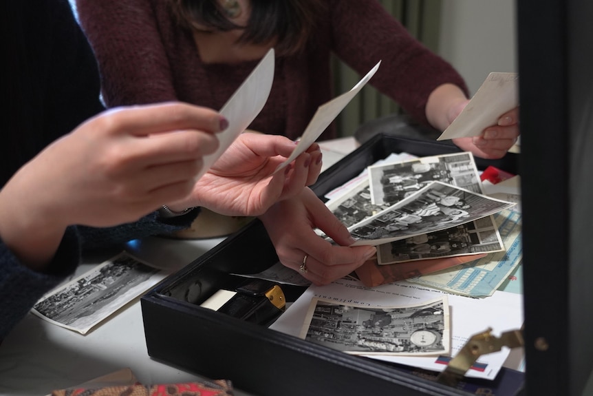 Two peoples' hands going through photos and documents in an opened briefcase.