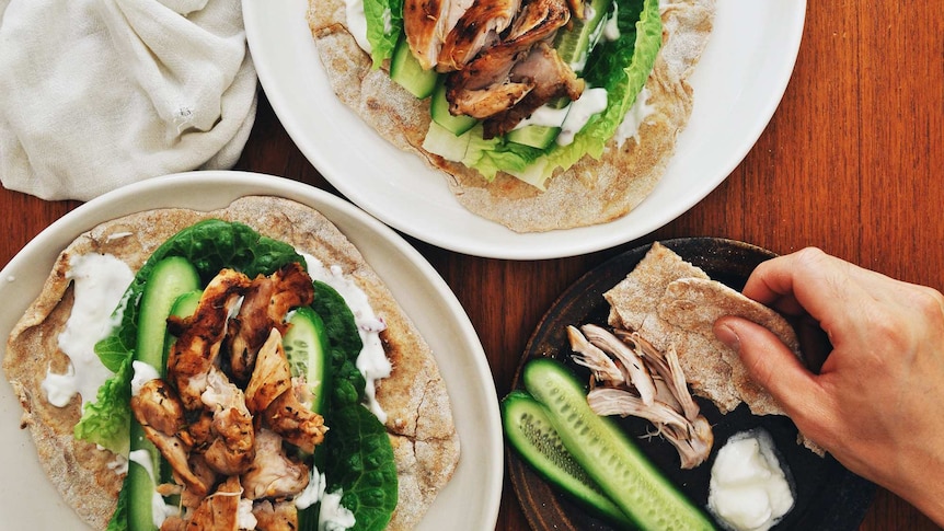 Two plates of grilled chicken served on flatbread with yoghurt sauce and vegetables, a satisfying family dinner recipe.