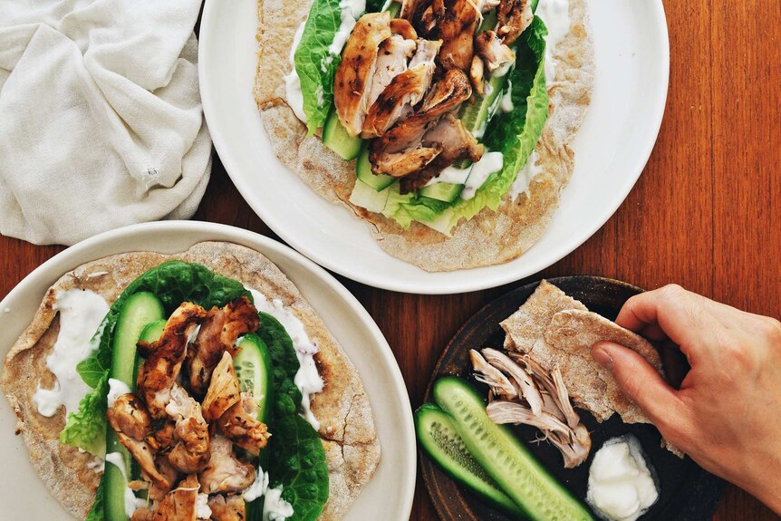 Two plates of grilled chicken served on flatbread with yoghurt sauce and vegetables, a satisfying family dinner recipe.