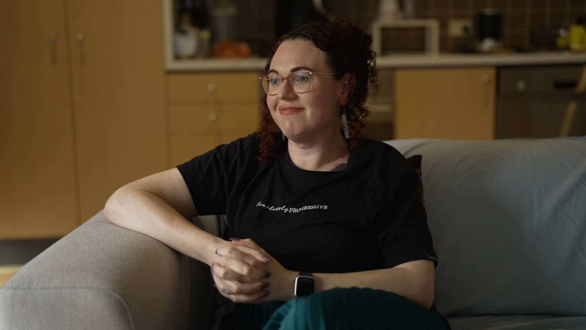 A woman wearing a black shirt sitting on the corner of a couch.