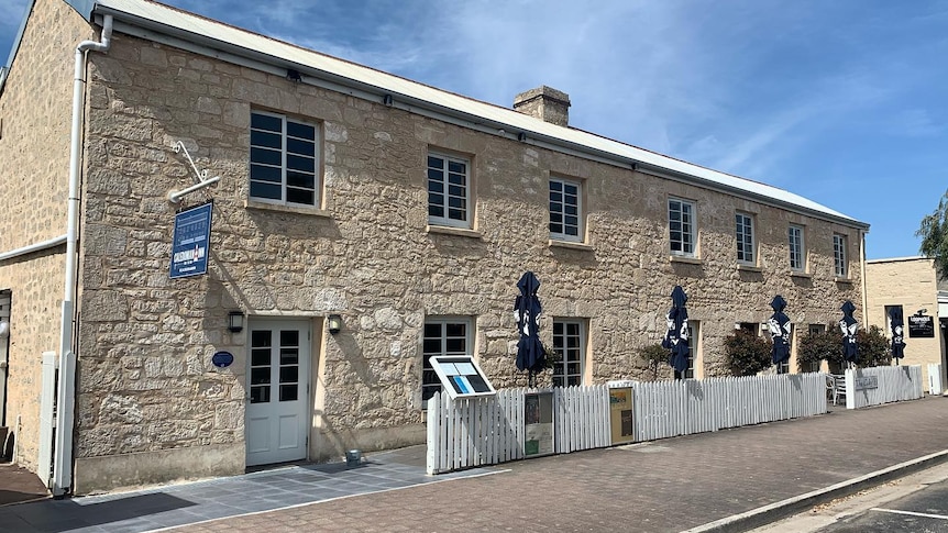 An old beige limestone building with windows and umbrellas out the front