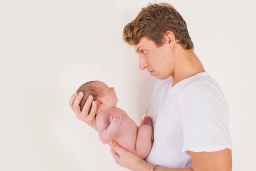 A man cradling and looking at with a newborn baby.