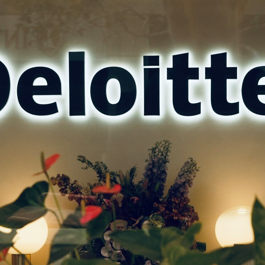 An illuminated Deloitte logo in a foyer with an arrangement of flowers beneath.