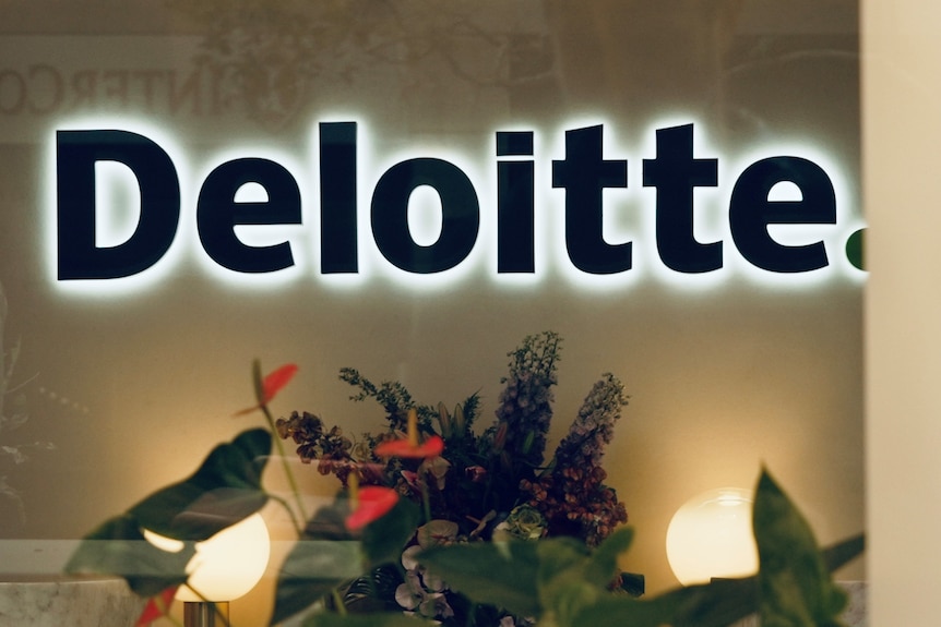 An illuminated Deloitte logo in a foyer with an arrangement of flowers beneath.