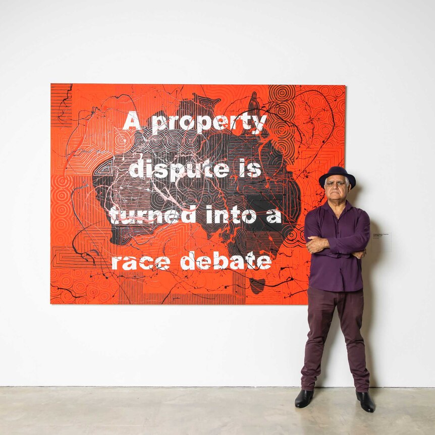 Richard Bell standing beside his artwork "A property dispute is turned into a race debate" (2019)