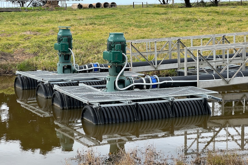 Two electric pumps float on a pontoon in the brown water of a farm dam.