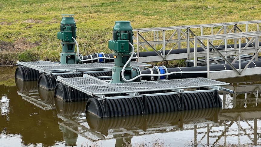 Two electric pumps float on a pontoon in the brown water of a farm dam.