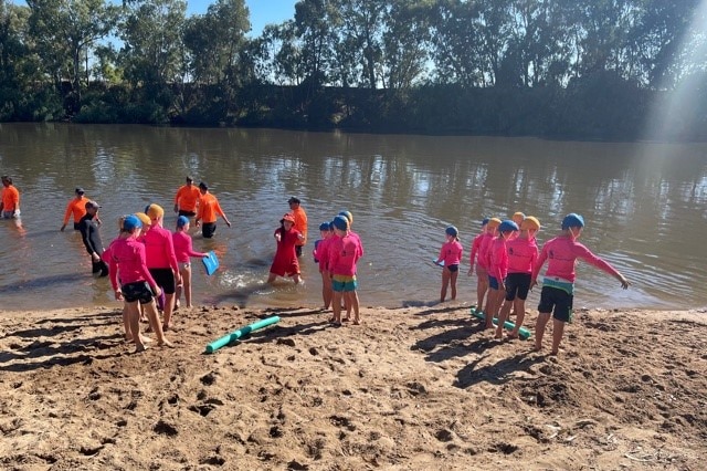 Kids in pink swim shirts walk into a river.