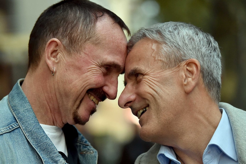 Karl Kreile and his partner Bodo Mende look into each others eyes and smile while pressing their foreheads together.