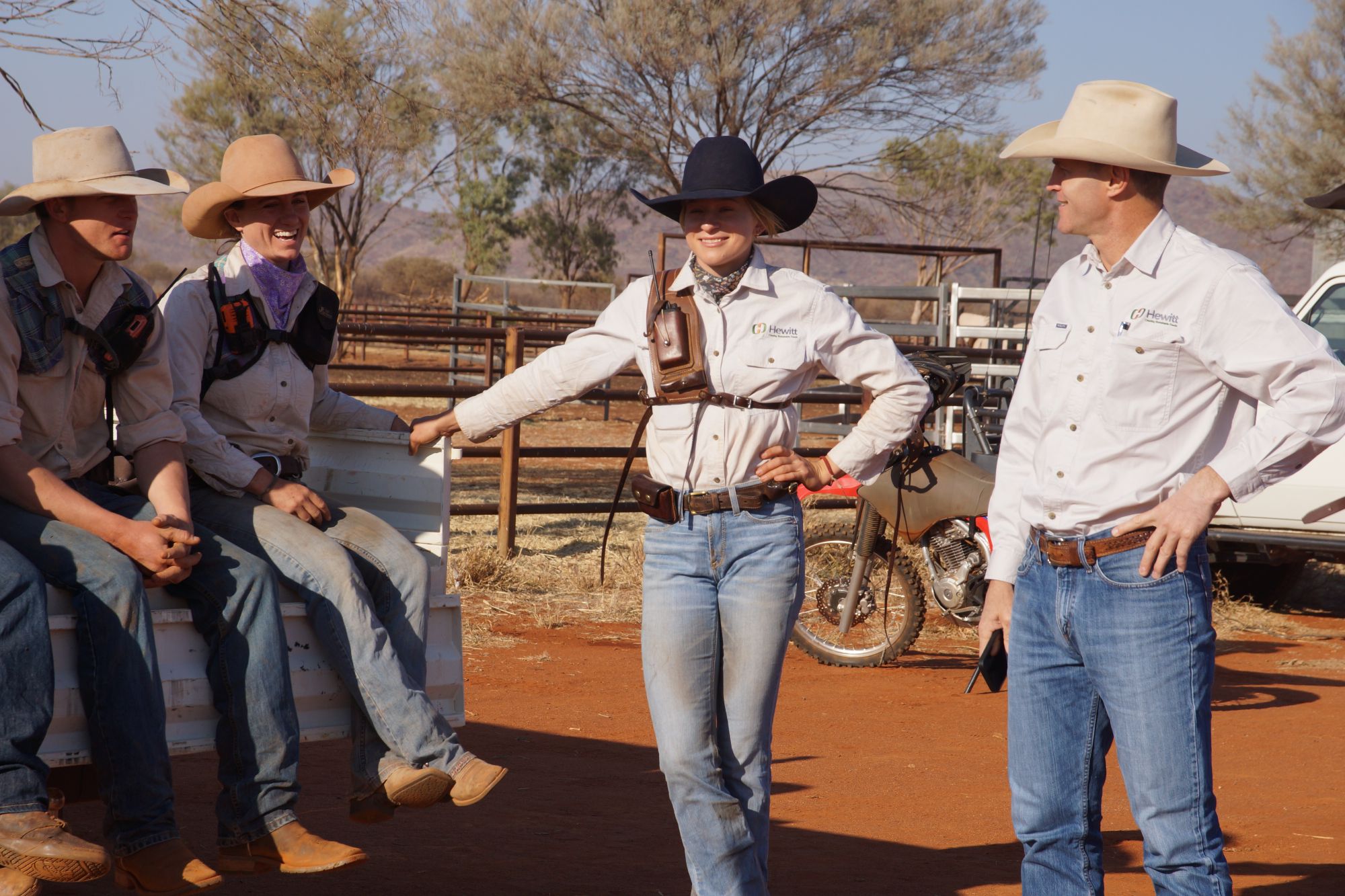 A group of people wearing cowboy hats and boots sit on and stand near a ute.