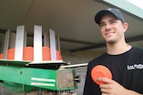 Sam Byslma holds an orange clay target in front of a clay target throwing machine