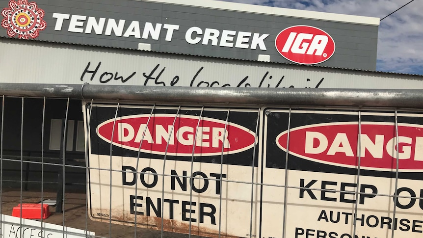 An IGA supermarket cordoned off by fences festooned with warning signs.