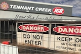 Danger do not enter signs on a fence, which is in front of a building. A sign on the building says Tennant Creek IGA.