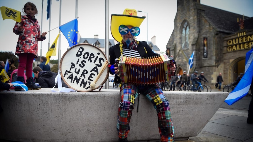A man in colourful clothes and an accordion sits next to a drum with the words 'Boris is a pure fanny'