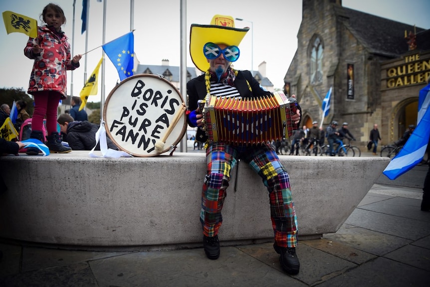 A man in colourful clothes and an accordion sits next to a drum with the words 'Boris is a pure fanny'