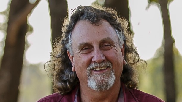 A man with shoulder-length grey hair and beard, smiling at camera