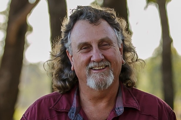 A man with shoulder-length grey hair and beard, smiling at camera