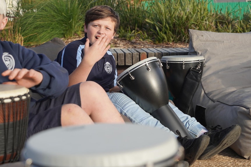 A young boy sits down playing a drum