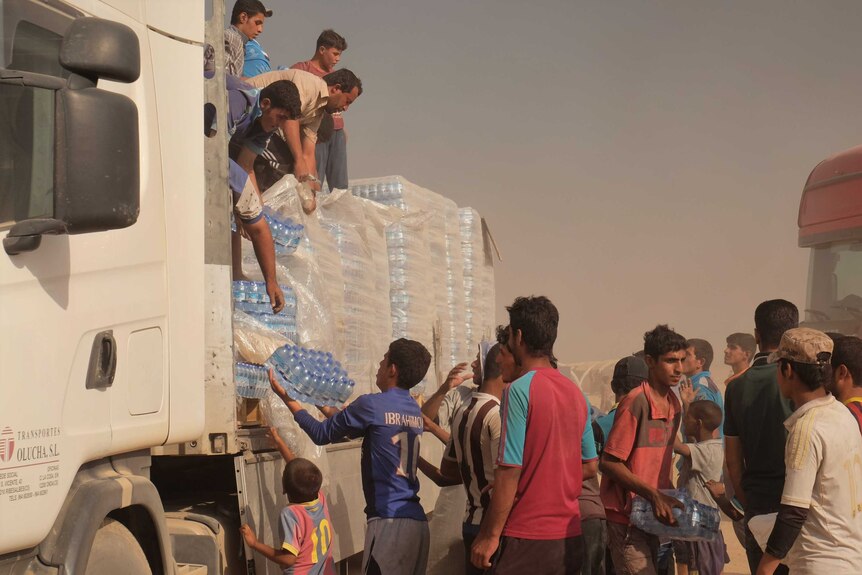 Men hand pallets of water from a truck to waiting people on the ground.