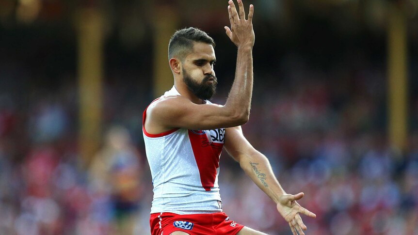 Sydney Swans player Lewis Jetta performing an Aboriginal dance with his arms on a football field.