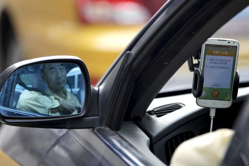 A taxi driver is reflected in a side mirror as he uses the Didi application.