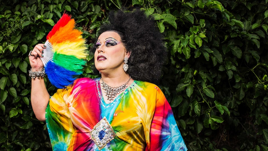 Colour photograph of drag performer Lasey Dunaman posing in front of a wall of vines.