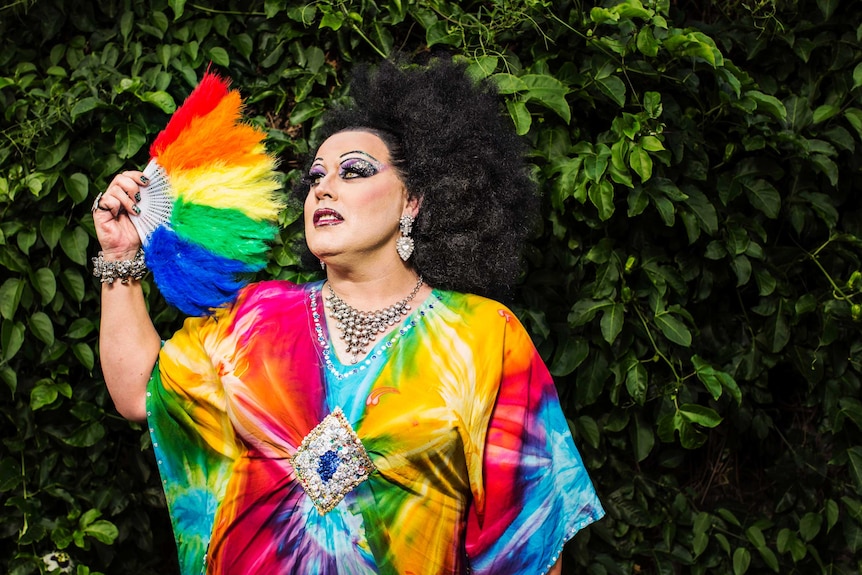 Colour photograph of drag performer Lasey Dunaman posing in front of a wall of vines.