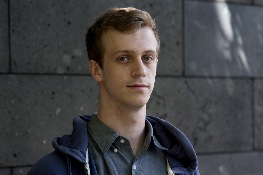 Darcy Phillips looks at the camera as he is photographed from the shoulders up in front of a wall.