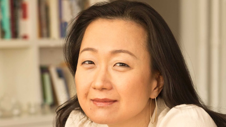 The author in front of a bookcase leans towards the camera