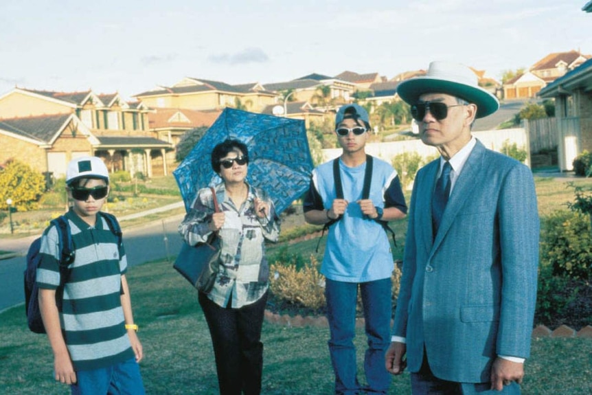 A family wearing sunglasses stands in a suburban front yard.