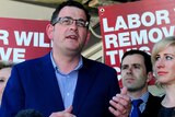 Daniel Andrews speaks to reporters in front of Labor campaign banners.