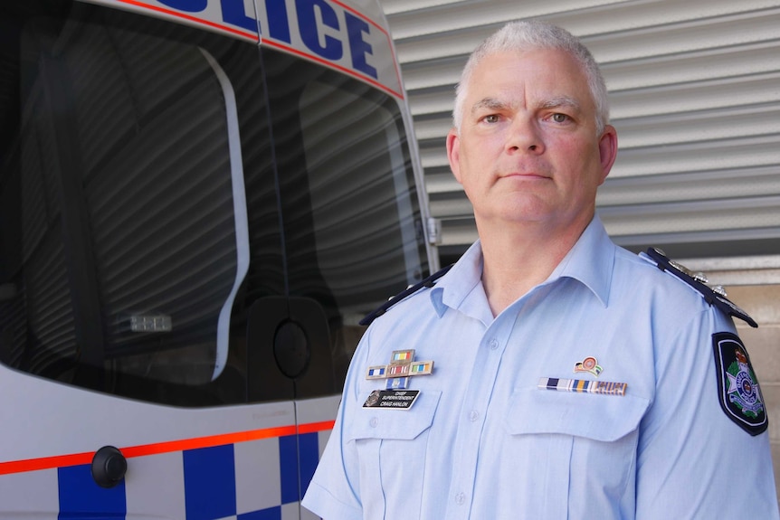 A police officer with close-cropped grey hair stands in front of a police van.
