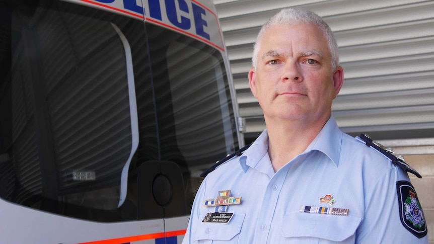 Senior police officer in front of police car.