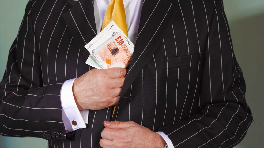 A man is putting cash into a suit jacket pocket