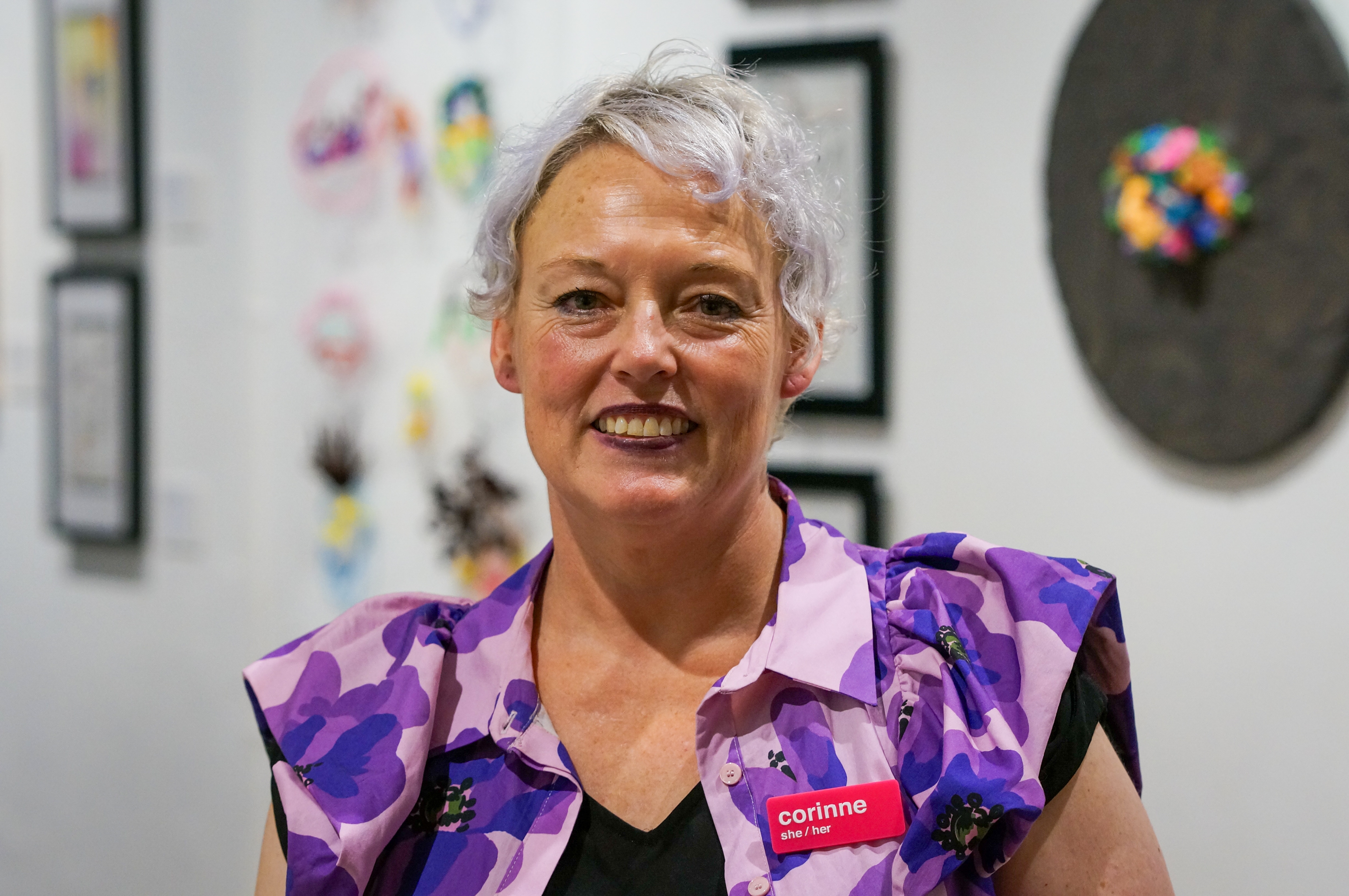 Женщина с короткими седыми волосами в блузке с короткими рукавами с рисунком. 