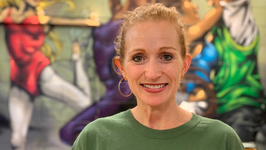 Ms Parnell smiles in front of a mural of people dancing.