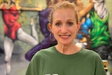 Ms Parnell smiles in front of a mural of people dancing.