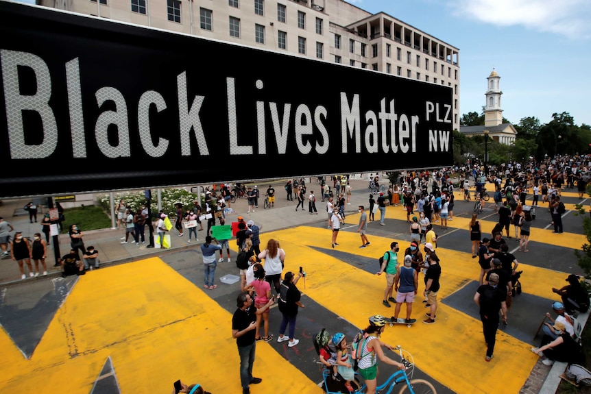 Crowds of people can be seen on a street with a sign for Black Lives Matter Plaza in the foreground