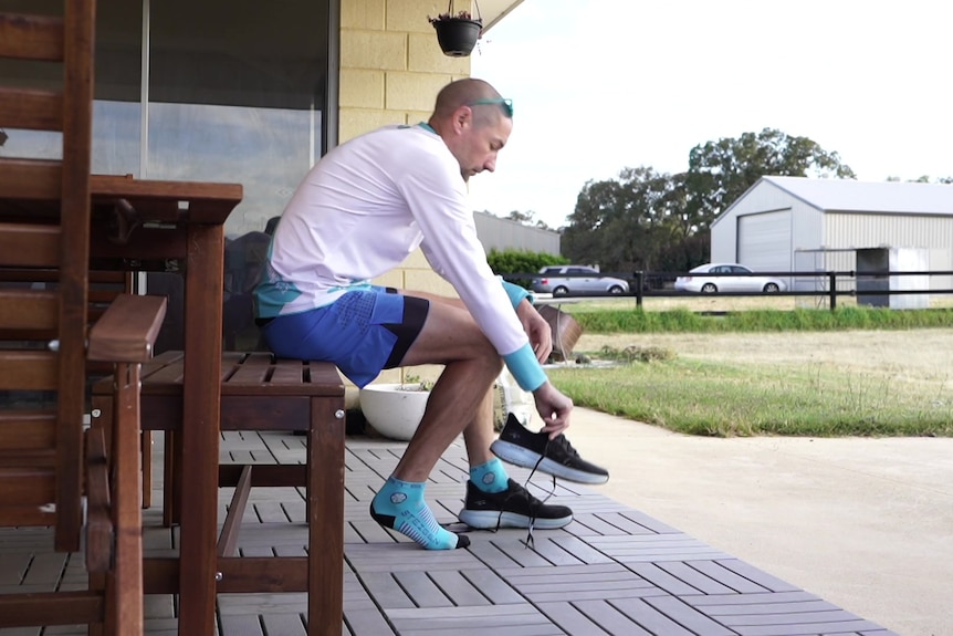 A man sits on a bench putting on a pair of running shoes. 