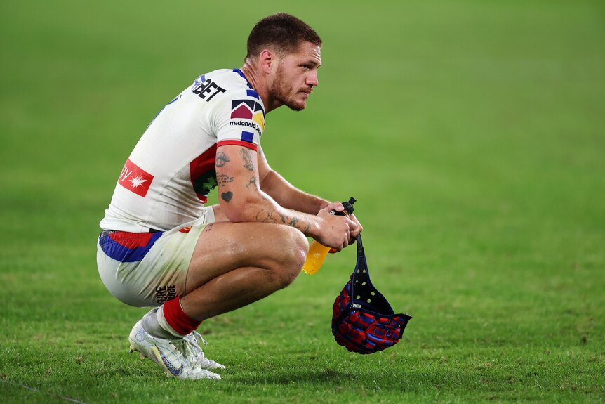 Newcastle Knights' Kalyn Ponga squats on the field, holding his headgear, after an NRL game.