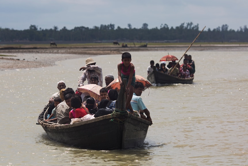 Refugees, crowded onto small wooden boats, cross a stream.